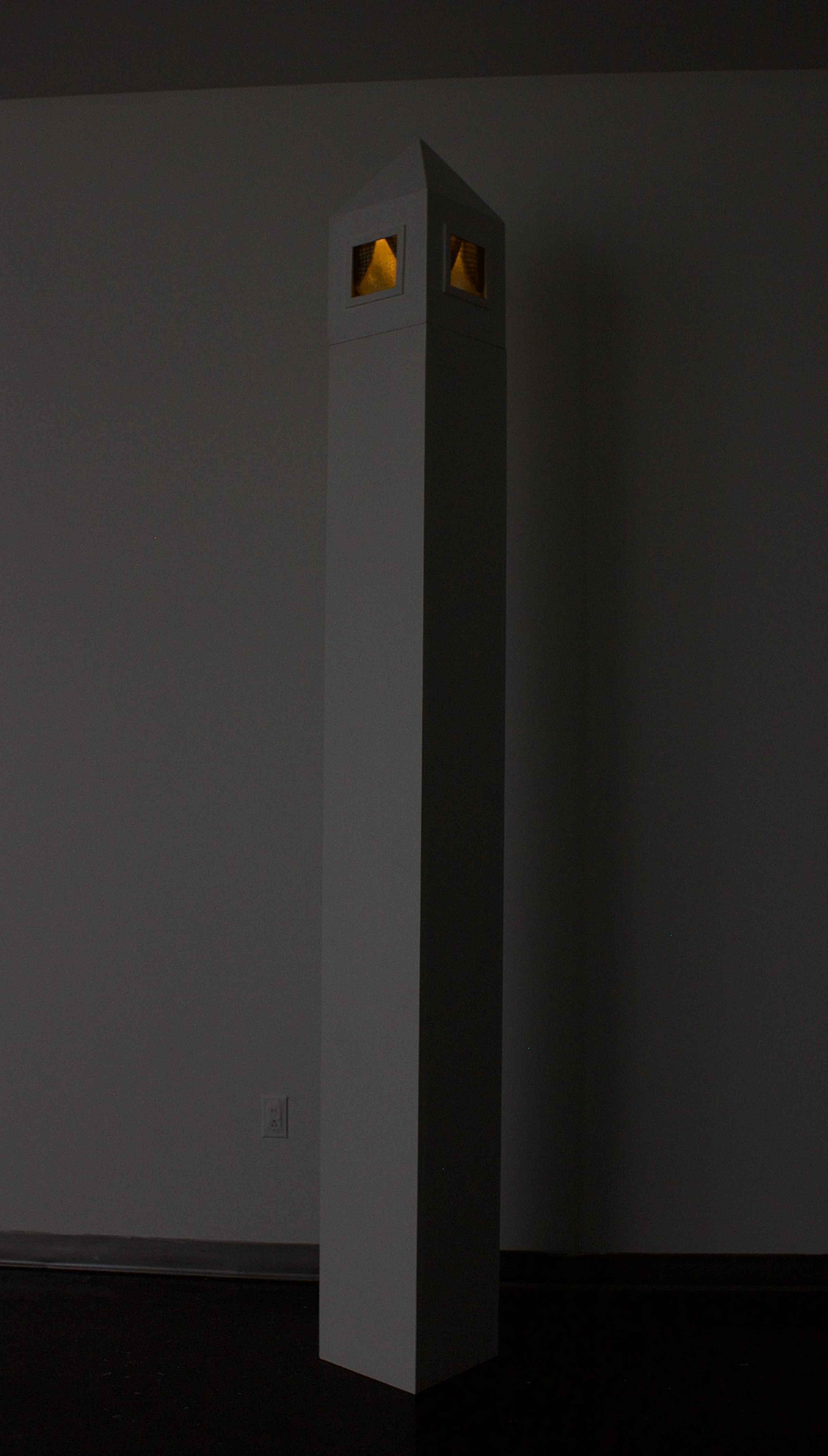 A tall square tower-like art piece, with windows inside near the top